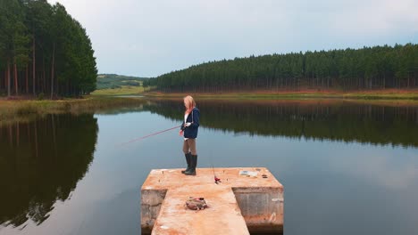 a girl fishing from a pier on a beautiful calm lake in a forest