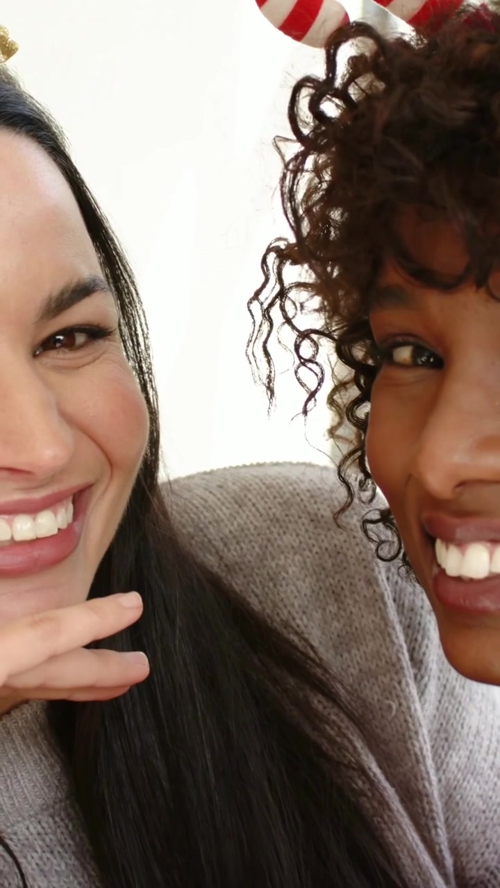 Video verticale: Donne che ridono che posano per un selfie natalizio a casa, indossando maglioni e fasce per capelli.