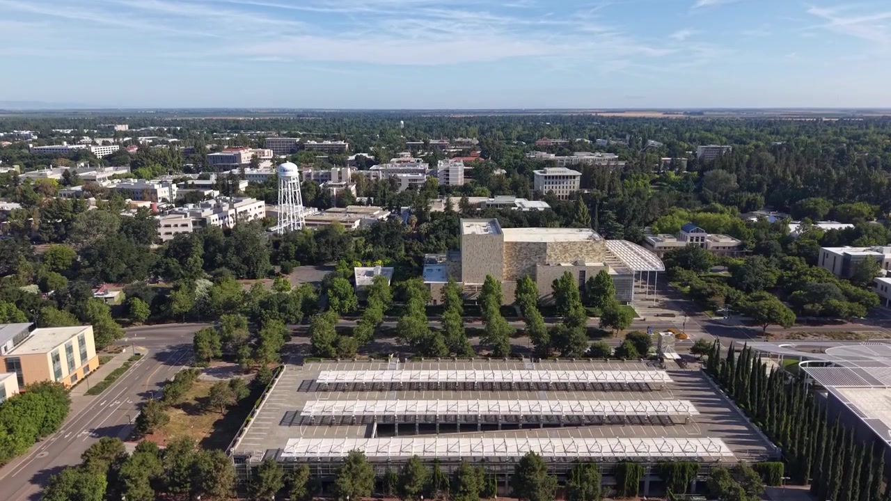 Ripresa aerea con drone in ascesa del campus dell'Università della California, Davis, che mostra il Robert and Margrit Mondavi Center for the Performing Arts e il paesaggio urbano circostante in una giornata di sole.