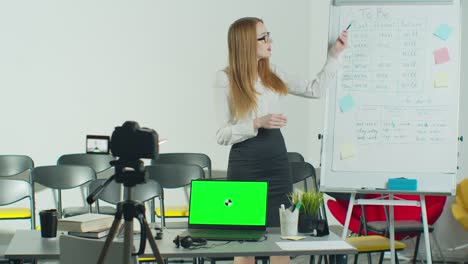 a woman is conducting an e-lesson from an empty classroom. remote education, online education, remote studying, online learning concept. green screen chroma key laptop for learning.