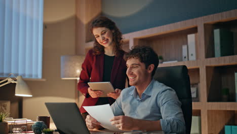 smiling teammates video calling looking laptop webcam in evening workplace.