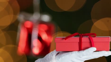 Animation-Des-Weihnachtsmanns,-Der-Ein-Weihnachtsgeschenk-über-Orangefarbenen-Lichtflecken-Hält