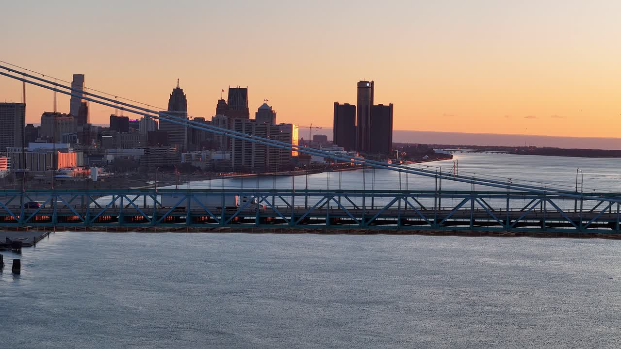 White truck crossing ambassador Bridge at sunrise with Detroit skyline and the river in the background