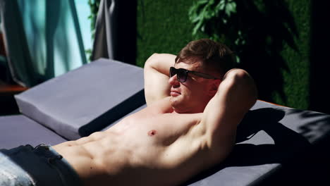 relaxed caucasian man lying on deck sunbathing. man holds his hands behind the head enjoying the sun.