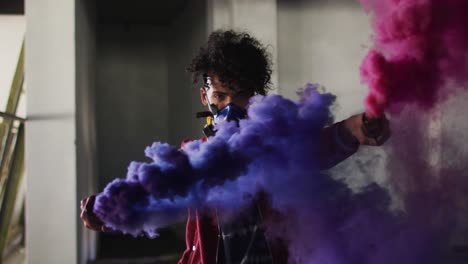 Mixed-race-man-holding-blue-and-purple-flares-standing-in-an-empty-building