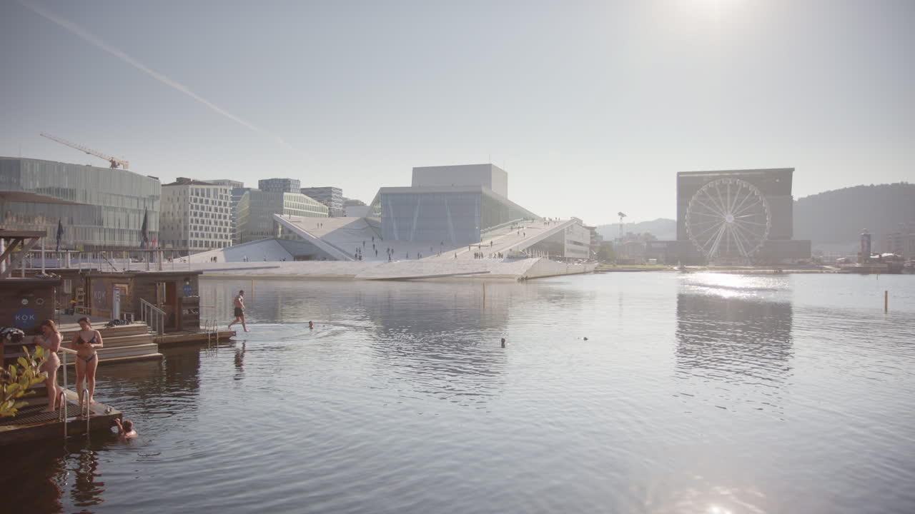 Floating saunas on Oslo harbour promenade waterfront, people diving into fjord