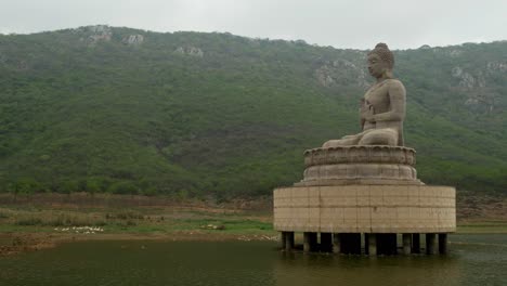 70 foot high buddha statue at ghora katora lake surrounded by mountains under hazy sky, rajgir, bihar, india