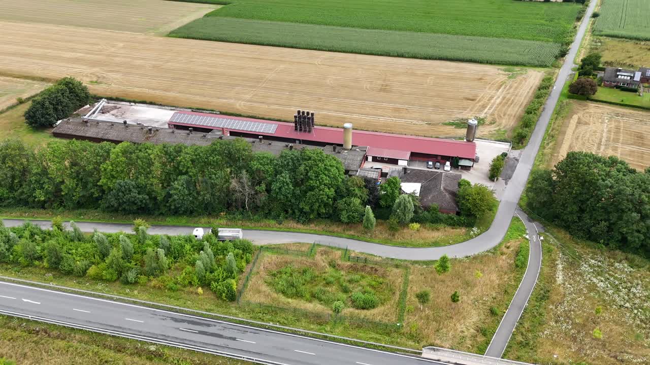 Traditional American barn in red color in rural area. Aerial lateral wide shot. Traffic on road. Sunny day in summer. Growing wheat, soy and corns on field. Peaceful neighborhood in Dakota