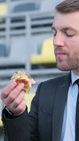 American Office Worker Having Lunch Outdoors he Eats a Sandwich while Sitting on a Bench a Young American Office Worker is Having Lunch Outdoors he is Eating a Sandwich while Sitting on a Bench Near an Office Building