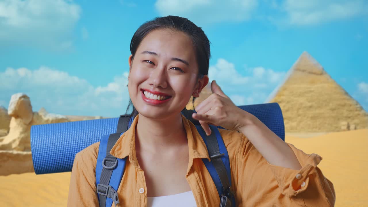 Close Up Of Asian Female Hiker With Mountaineering Backpack Smiling And Showing Call Me Gesture While Traveling In Pyramid Of Giza