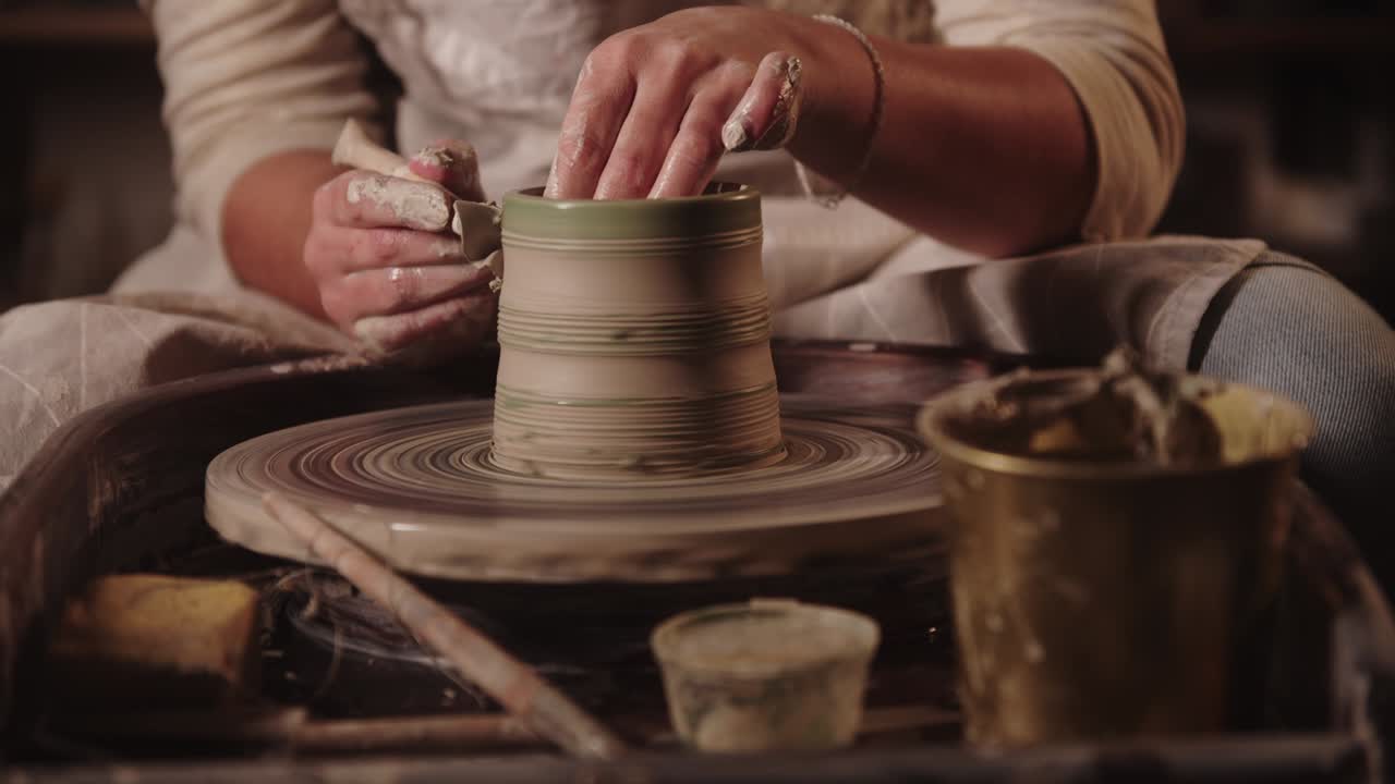 молодая женщина-ковчег отрезает избыток из глиняного горшка на колесе