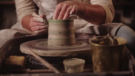 young woman potter cutting off the excess out of clay pot on the wheel