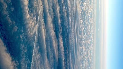 amazing view from cockpit of flying airplane above clouds leaving long white condensation vapor air trail in blue sky, zoom out vertical format