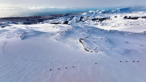 Vista-Aérea-Del-Paisaje-De-Personas-Montando-Motos-De-Nieve-En-El-Suelo-Helado-Del-Glaciar-Myrdalsjokull-En-Islandia,-Al-Atardecer