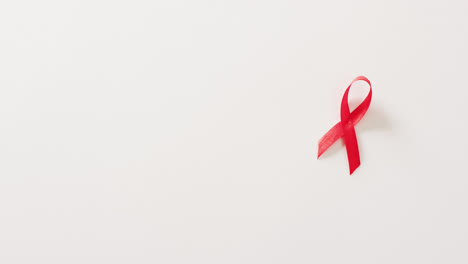 Video-of-red-hiv-or-aids-awareness-ribbon-on-white-background-with-copy-space