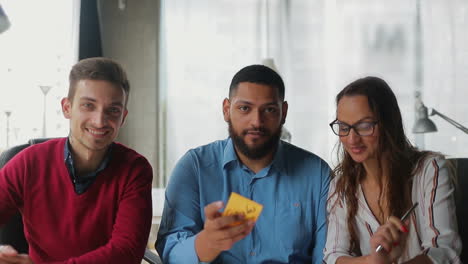 Smiling-young-people-showing-sticky-notes-and-waving-to-camera.