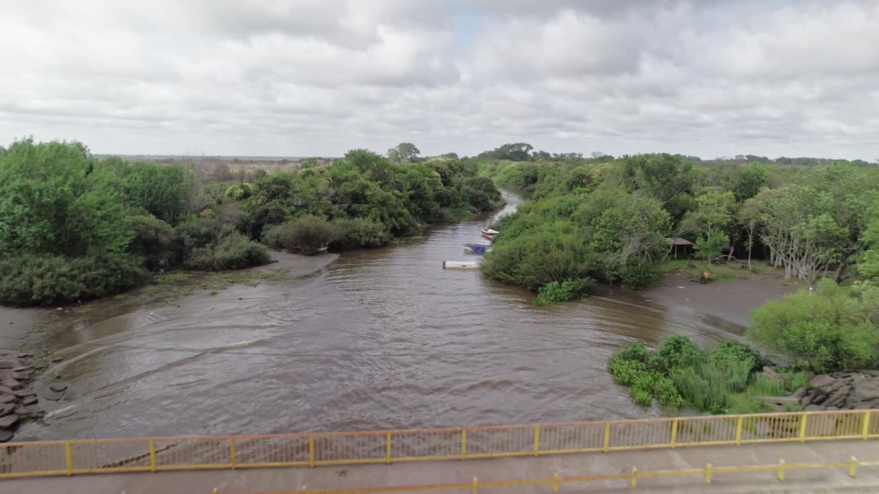 The drone follows the winding river through dense greenery in Punta Lara, Buenos Aires, capturing the natural landscape with boats along the riverbank.