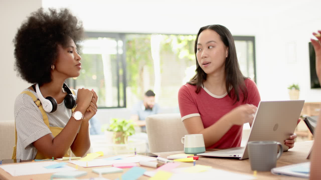 Discussing ideas, diverse friends collaborating with laptop and sticky notes in workspace