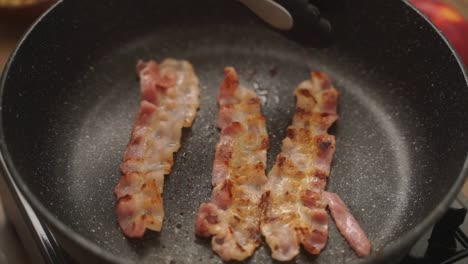 persona de la cosecha girando tocino frito en la sartén