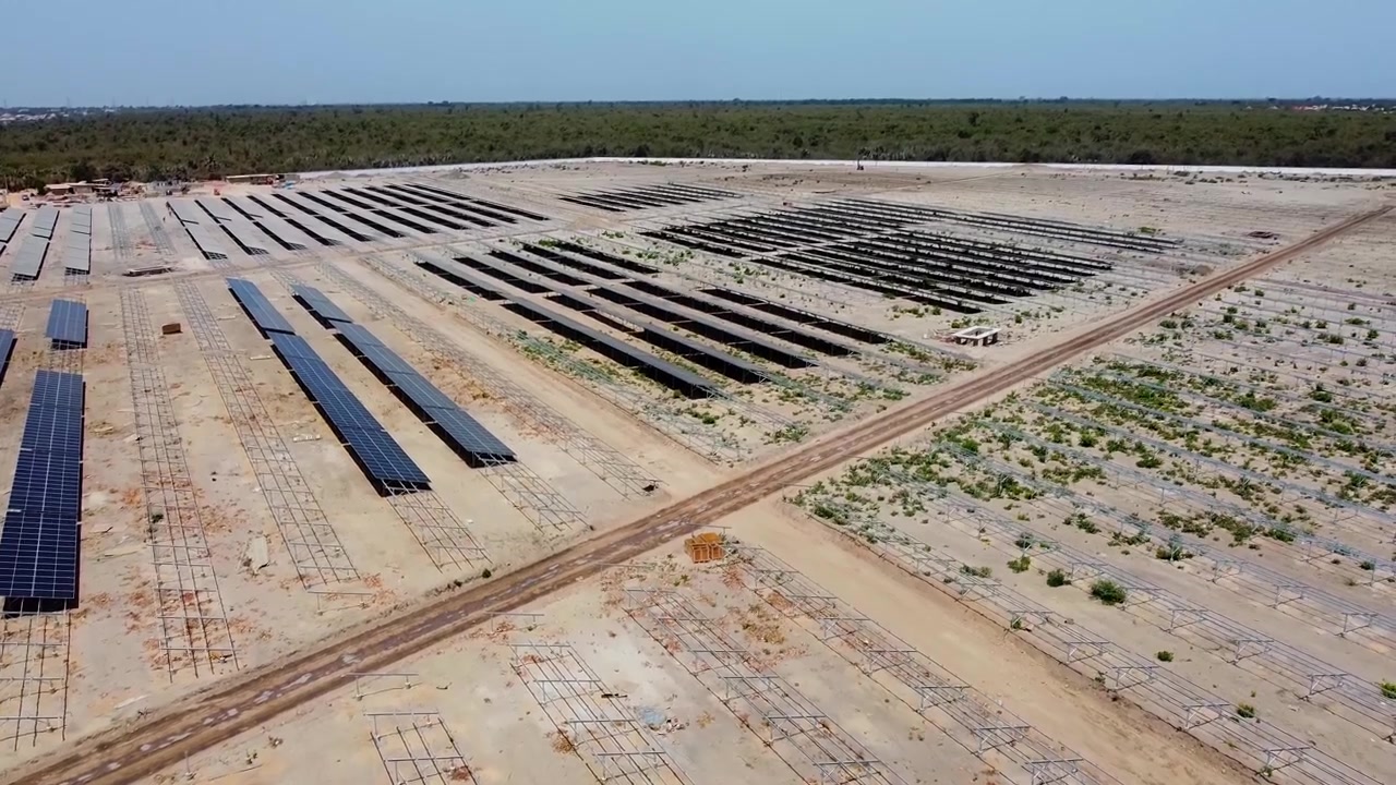 Ampia vista aerea a volo d'uccello con movimento tilt-up di nuovi pannelli solari e telai di supporto presso la centrale solare di Jambur in costruzione.