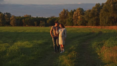 pregnant couple walking in a field at sunset