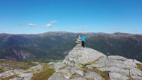 man standing on mountain peak with raised arms to celebrate achievement reaching the top - orbiting aerial with parallax effect and norway mountain landscape in background