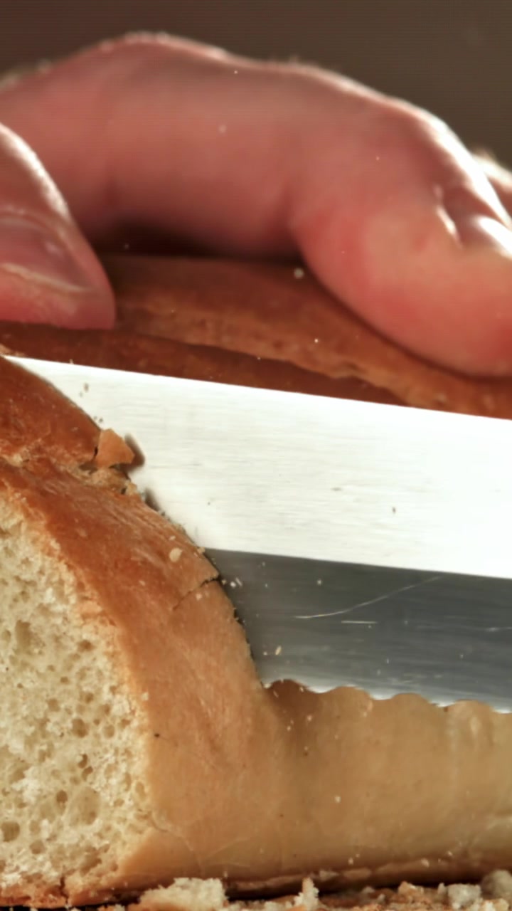 Slow Motion Close-Up of a Serrated Knife Slicing Fresh Bread