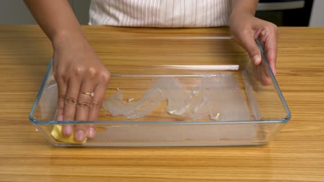 married female rubbing in glass cooking tray with butter for cooking