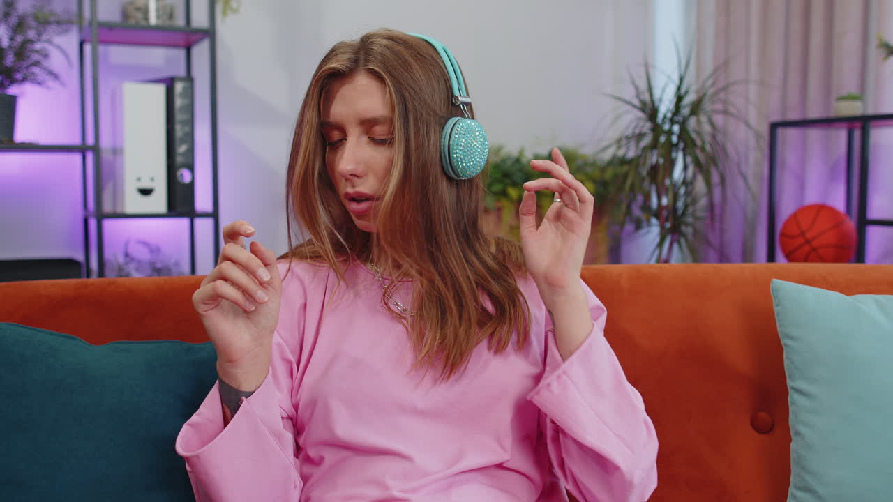 chica feliz y relajada con auriculares inalámbricos bailando escuchando su música rock n roll favorita en el sofá de casa
