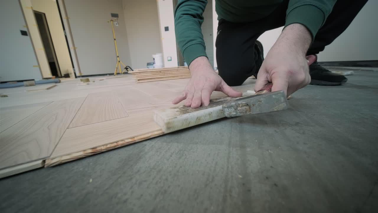 Worker installing wooden flooring with hammer and tapping block