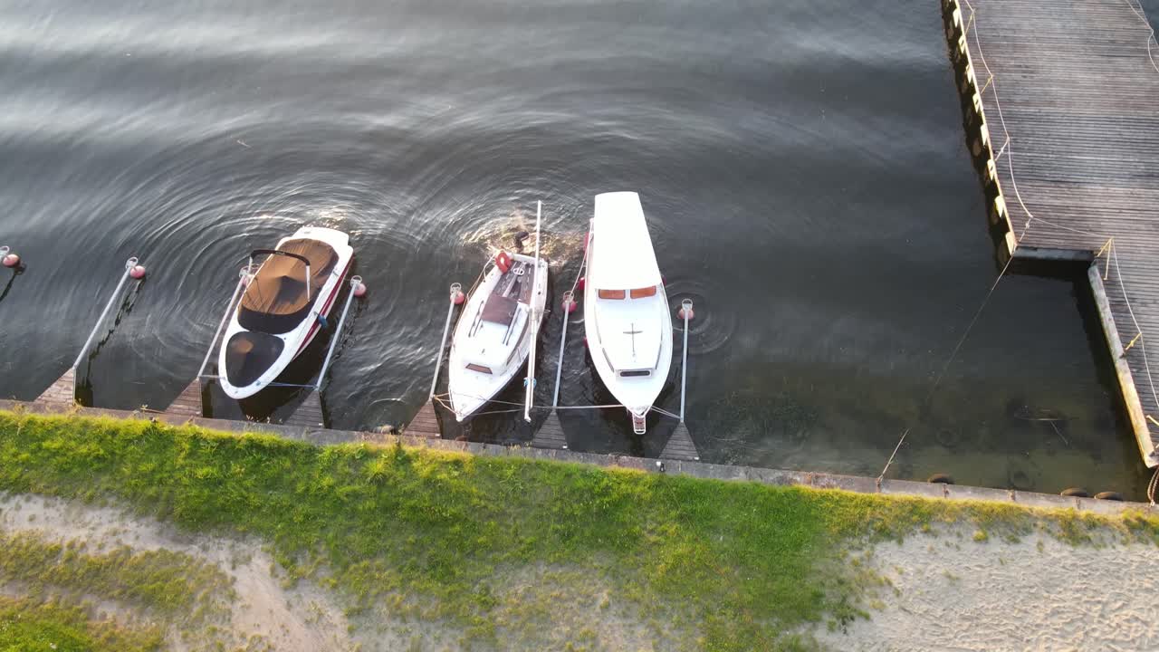 Aerial shot of moored boats and a wooden pier at sunset. The golden sunlight reflects beautifully on the still lake surface, creating a calm and scenic atmosphere.