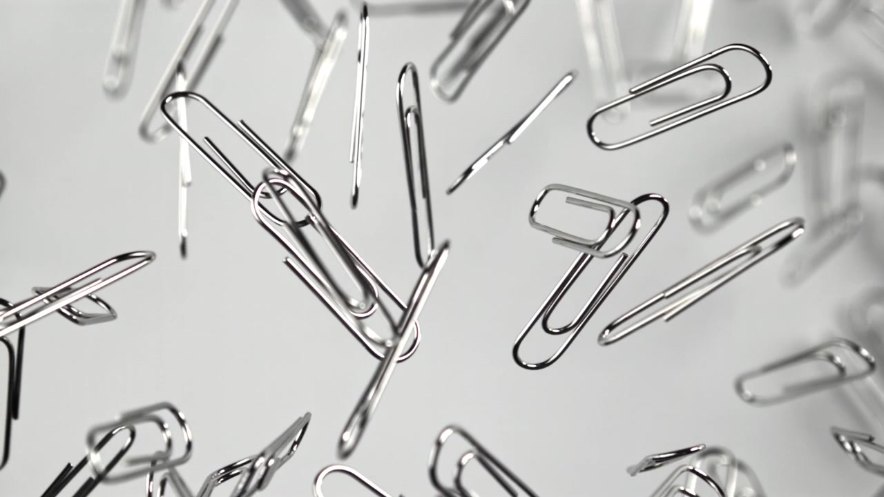 Silver Paper Clips Falling in Slow Motion Against a White Background