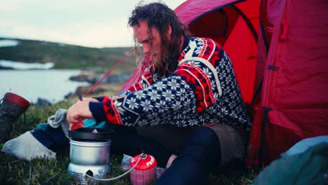 a man is preparing a meal on his portable stove at the lakeshore of mefjellsvatnet in indre fosen, trøndelag, norway - close up