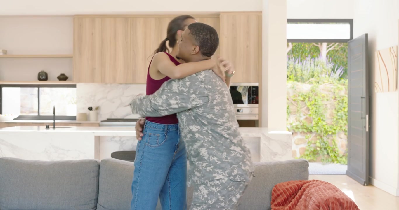Coppia afroamericana, la porta di casa si apre, un soldato in uniforme torna con un borsone e si abbracciano.