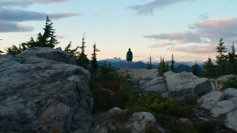 aerial push in past a person watching sunset from top of the mountain