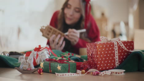 christmas presents and ornaments on floor with woman coloring cardboard house at home