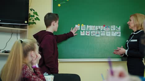 back to school. female teacher and a schoolboy near the blackboard. student speaks in the classroom while looking on pictures on chalkboard. education at school.