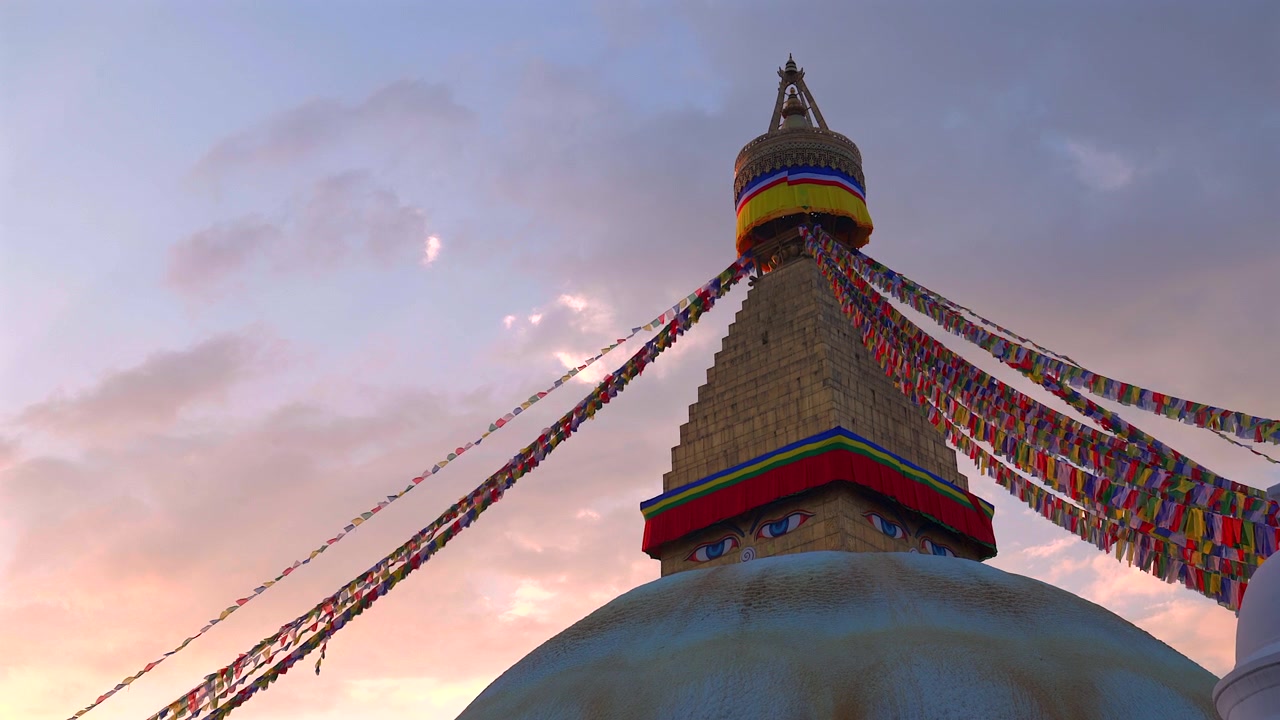 Matala staattinen kuva Boudhanathin stupan kultaisesta tornista ja Buddhan silmistä liehuvien rukouslippujen kera kaunista vaaleanpunaista ja violettia auringonlaskun taivasta vasten Kathmandussa, Nepalissa.
