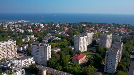 aerial backwards shot of residential apartments in park of gdynia with blue baltic sea and cruising ships in background