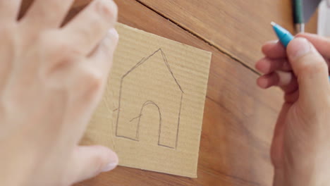 close up of hand drawing a house on cardboard