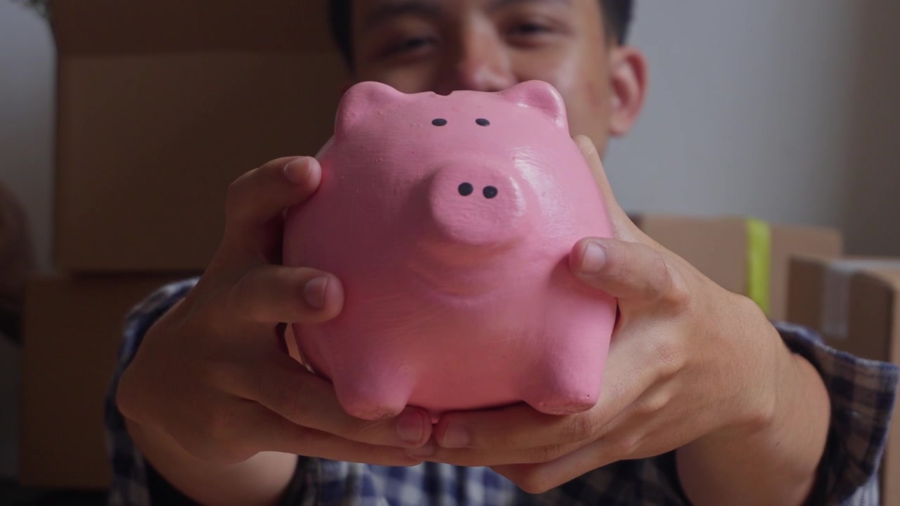 Joven sonriente mostrando una hucha hacia la cámara.