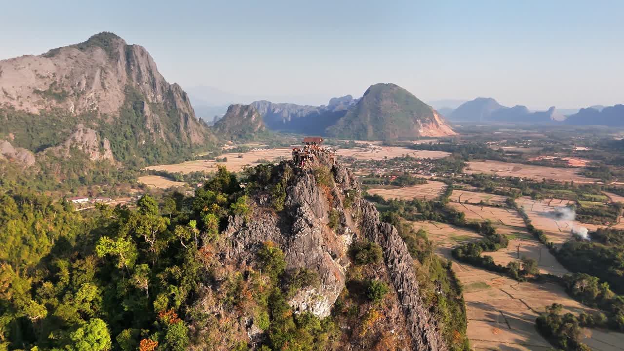 Drone orbit of jagged karst peaks above Nam Song River valley near Vang Vieng, Laos, showing Phou Pha Dang ridge and surrounding limestone mountains in golden evening light