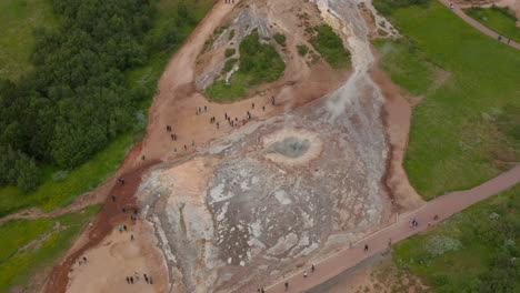 Aerial-view-of-active-geothermic-geysir-in-highlands-of-Iceland.-Drone-view-of-touristic-icelandic-landmark-with-steaming-craters-of-hot-water-and-tourist-visiting.-Geyser-valley