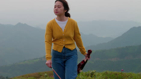 woman with violin walking on a hill, overcast, mountains visible in background