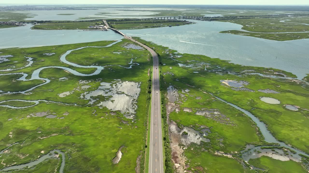 Driving cars on road between marshland and wetland of New Jersey. Bridges over river bay water in summer. Aerial panorama wide shot. Atlantic Ocean in distance