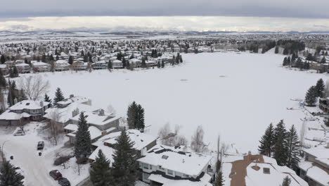 Homes-around-a-frozen-lake-in-the-prairies-in-Alberta,-Canada-frozen-from-a-drone