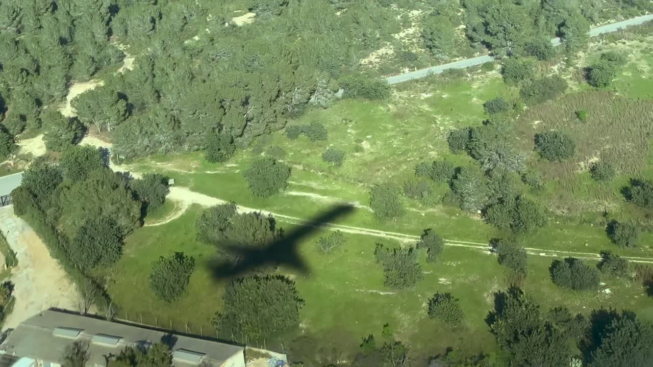 Cockpit-Luftaufnahme vom Schatten eines mittelgroßen Düsenflugzeugs am Boden im Endanflug, das eine Autobahn kreuzt.
