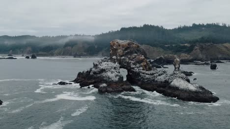 waves crashing on craggy rock formation at indian beach oregon on a foggy day