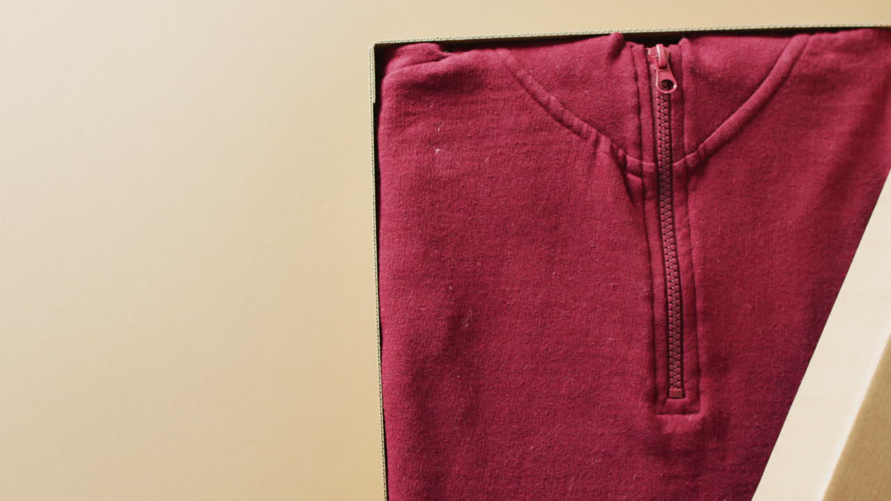 Video of close up of red sweater in box on beige background