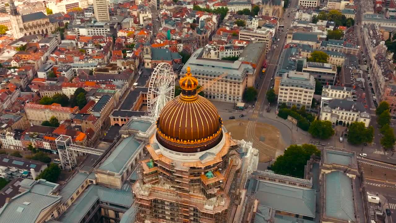 Aerial drone footage orbiting and spinning around the golden colored dome and rooftop of Court of justice or palace of justice in Brussels Belgium during a cloudy day with medieval buildings around it